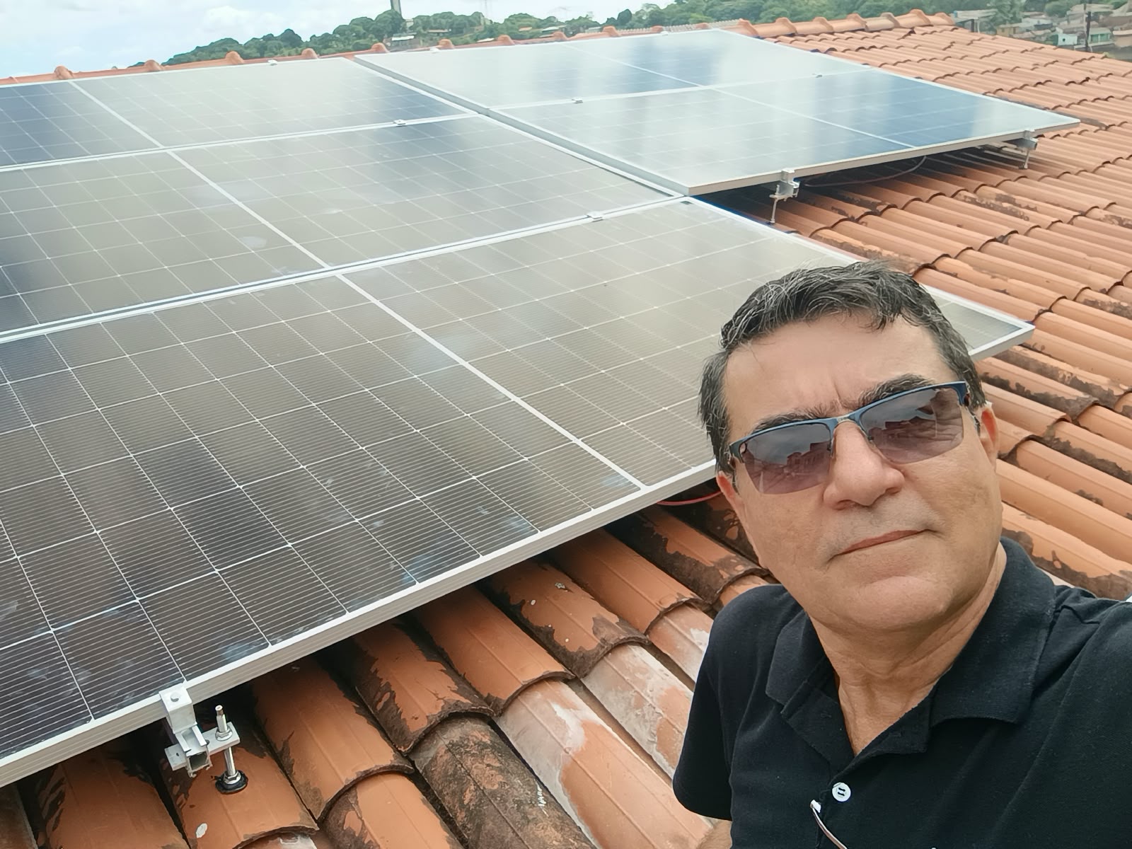 João Luiz junto a uma instalação de painéis solares em um telhado.